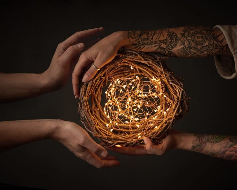 The hands of a woman with a tattoo and the men's hands hold a festive wreath with fringes around